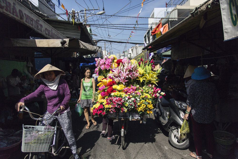 Shoppers walk past a flower vendor at a street market in Ho Chi Minh City, Vietnam.  Photographer: Ore Huiying/Bloomberg